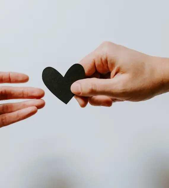 Persona entregando un corazón de papel negro